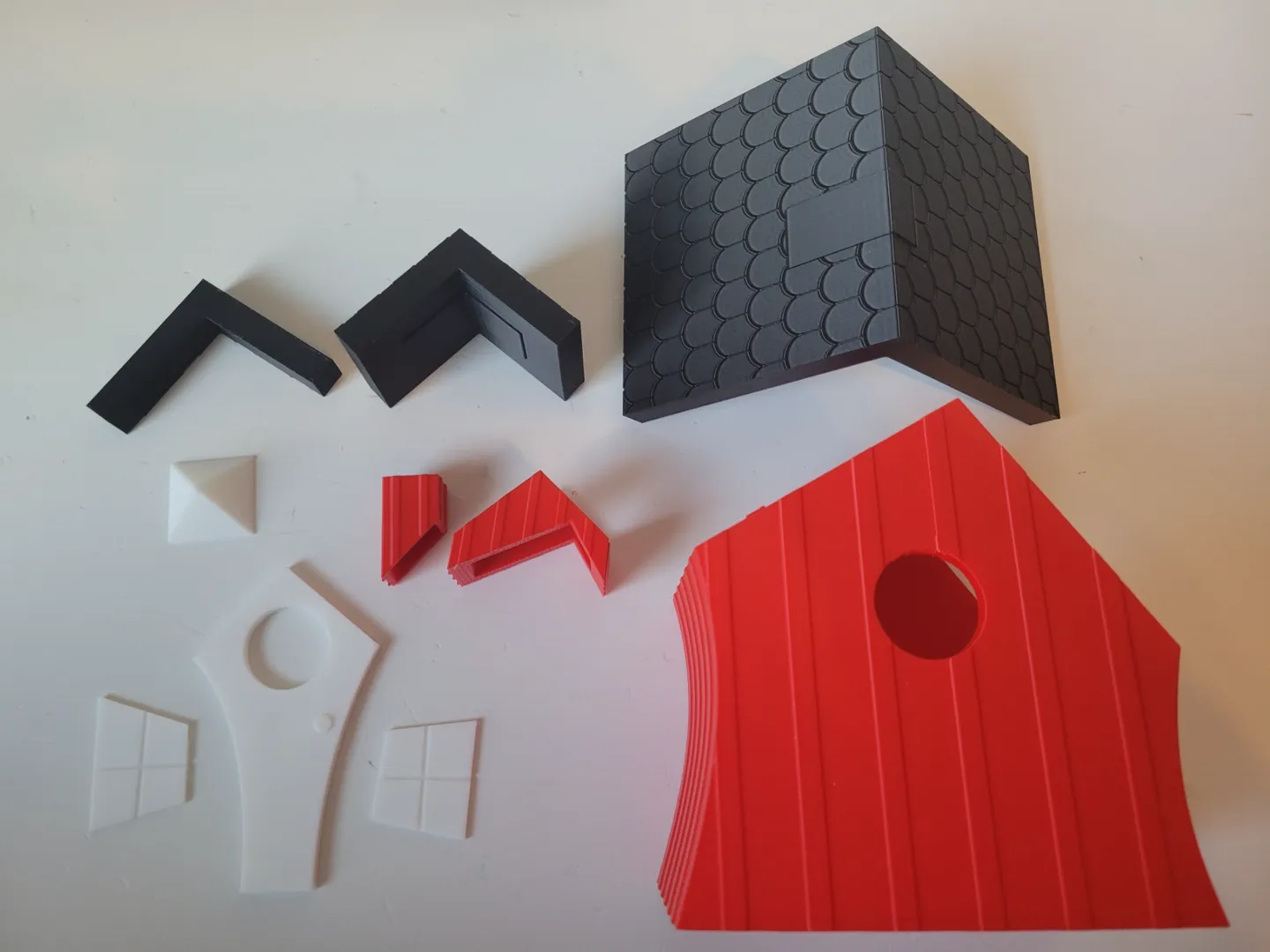 Disassembled red, white and black 3D-printed birdhouse parts laid out for assembly