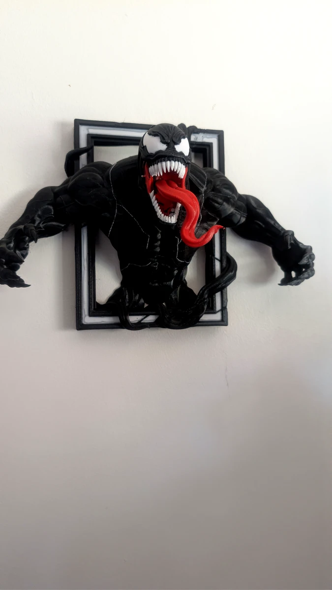 Venom character bursting out of a black wall-mounted picture frame, viewed from the front