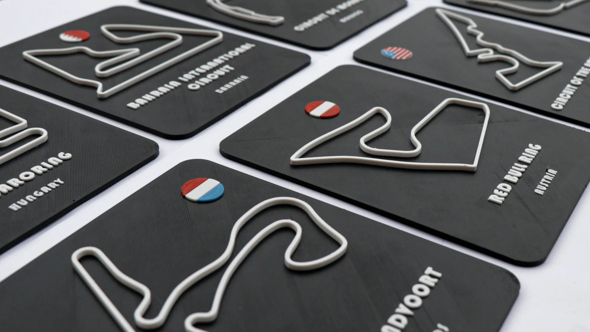 A collection of black 3D-printed plaques displaying raised outlines of Formula 1 circuits