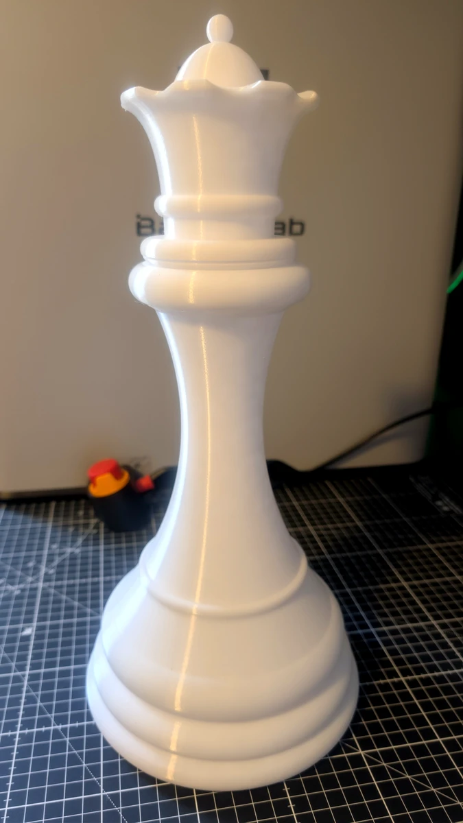 Raw white 3D-printed queen piece sitting on a workshop cutting mat